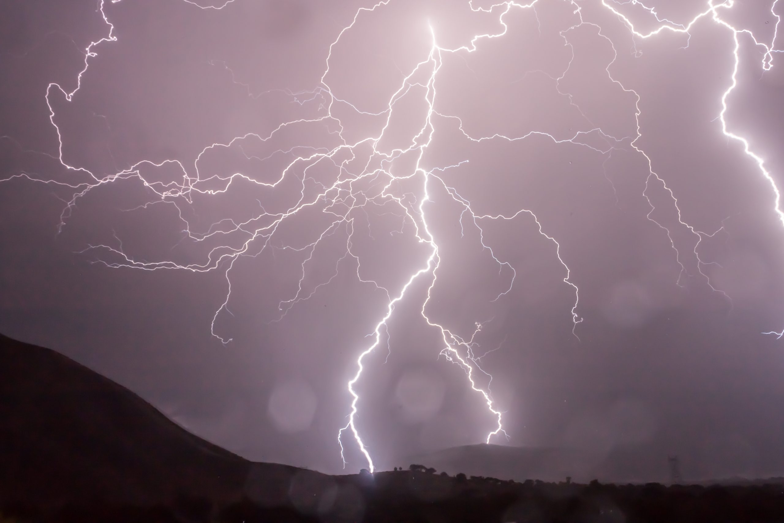 image shows lightning at night behind a landscape of mountains and valleys